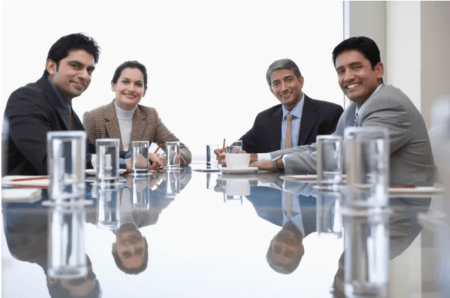 Business team meeting around a glass table, smiling and engaged.